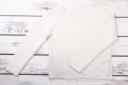 Beautiful female sweater, top view. Women white woolen sweater on wooden table. Female winter fashion outfit.の写真素材