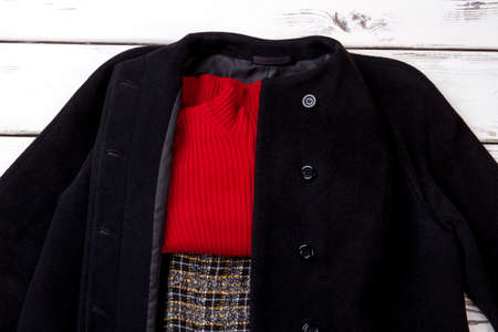 Set of female autumn apparel. Female black coat, red sweater and skirt on white wooden background....