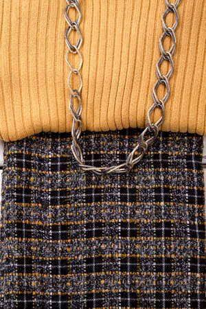 Close up female sweater and skirt. Detail of beige sweater and dark skirt. Women clothes and chain....