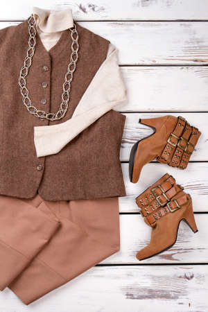 Set of elegant female clothes. Women vest and sweater. Female trousers and boots on vintage wooden background. Ladies classic outfit.の写真素材