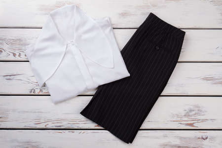 Set of female formal clothes, top view. Women black skirt and white blouse, wooden background. Ladies business style outfit.の写真素材