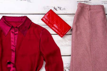 Female classic clothes and red purse. Feminine red shirt, skirt and leather wallet on white wooden background.の写真素材