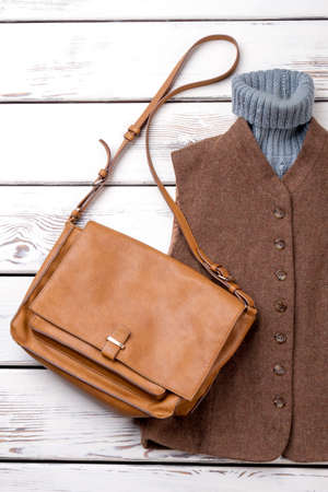Female fashion clothes and handbag. Women brown waistcoat and sweater, leather bag on wooden background. Flat lay women fashion outfit.の写真素材
