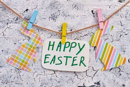 Easter greeting card and paper rabbits. Colorful Easter bunnies cut from paper and craft paper with text Happy Easter hanging on grey textured background. Handicrafting for Easter holidays at home.の写真素材