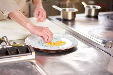 Male hands putting orange segments on plate. Chef at restaurant serving plate with orange pieces. Cook decorating plate with fresh orange.の写真素材
