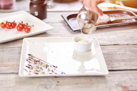 Cream pouring in porcelain dish. White sauce pouring into little porcelain pot. Restaurant and culinary concept.の写真素材