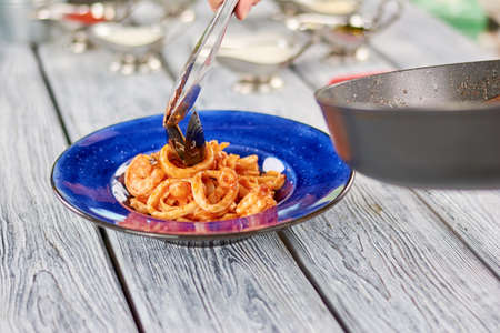 Kitchen stainless tongs putting mussel on pasta. Chef preparing an appetizing italian dish. Cooking and food concept.の写真素材