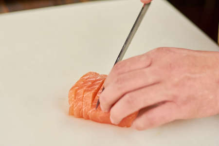 Chef hand slicing salmon close up. Male chef cutting raw salmon on cutting board. Chef at work, kitchen.の写真素材