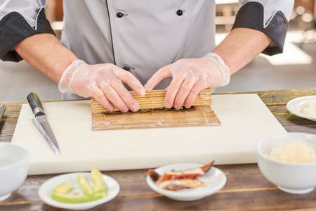 Cook making a sushi roll with bamboo mat. Chef sat professional kitchen preparing sushi. The process of sushi roll preparation.の写真素材