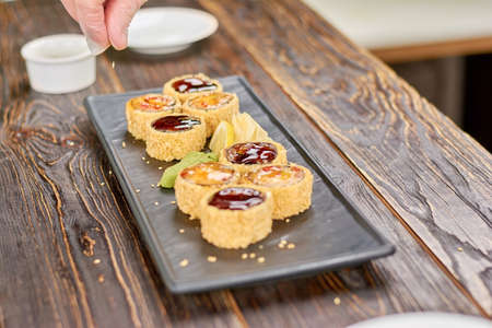 Chef adding sesame to sushi rolls. Delicilous set of unagi sushi rolls on plate. Restaurant of japanese food.の写真素材