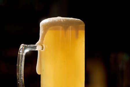 Light beer with foam on dark background. Glass of fresh cold beverage on pub background. Light beer...