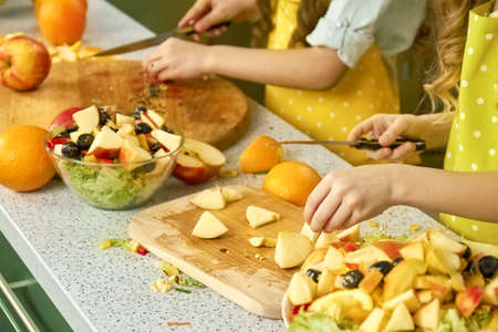 Hands of child cutting vegetables. Salad bowl, pieces of apple.の写真素材