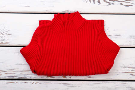 Horizontally folded red sweater. Bended pullover, bright wooden desk background.の写真素材