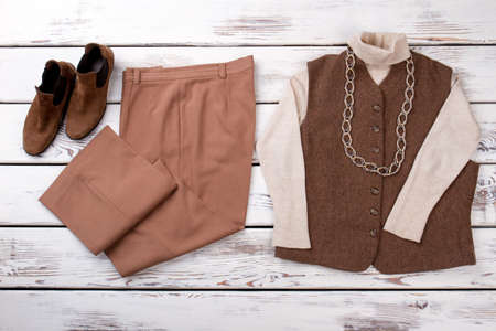 School winter suit on wooden table. Suede brown shoes, trousers and coat with white sleeves and chain necklace.の写真素材