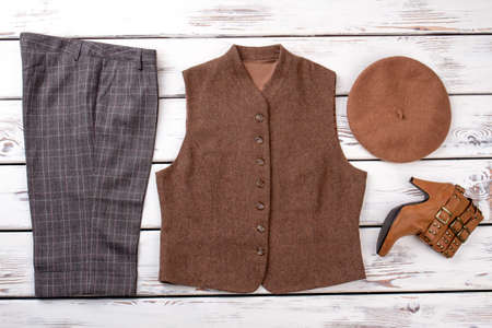 Fashionable female set of winter clothes. Grey trousers, brown jacket, hat and boot. Bright beige white wooden desks surface background.の写真素材