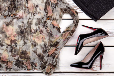 Shiny heel shoes and colourful fancy blouse. White wooden desks surface background.の写真素材