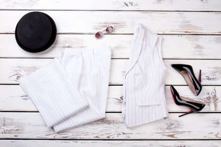 White womens suit, flat lay. Black high heel shoes and hat. Wooden desks surface background.の写真素材