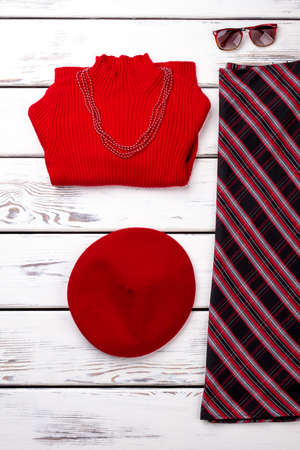 Red winter womens clothing. Folded sweater with necklace, berete hat, skirt and sunglasses.の写真素材