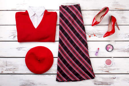 Red womens winter clothes look on wooden background. Flat lay. Folded shirt, sweater, shoes and cosmetic for make up.の写真素材