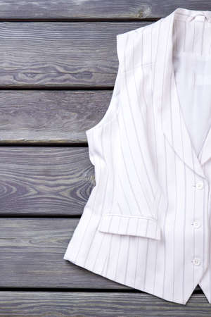 Close up white sleeveless business jacket. Vertical view, wooden desk surface background.の写真素材