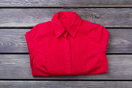 Red folded shirt. Top view, flat lay. Wooden desk surface background.の写真素材
