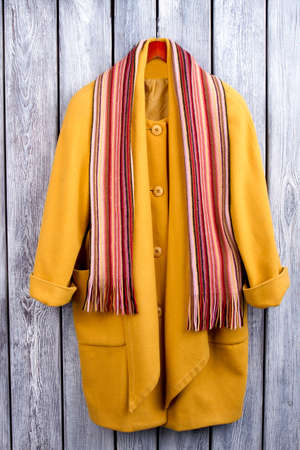 Flat lay yellow coat and scarf. Wooden desk surface background.の写真素材