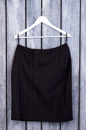 Black folded striped trousers on hanger. Front view. Grey wooden desk surface background.の写真素材