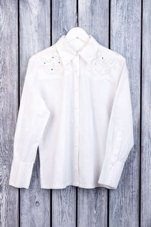 White decorated stylish woman shirt. Beautiful blouse on wooden desk surface, flat lay.の写真素材