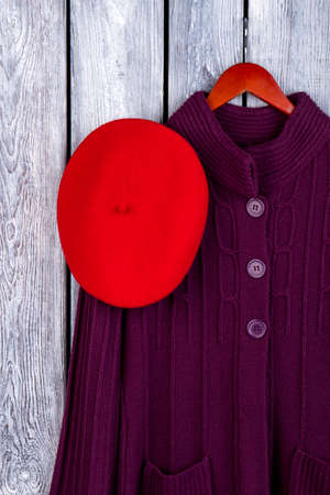 Fashionable lady winter clothes. Top view red hat and knitted coat on hanger. Dark wooden desk surface background.の写真素材