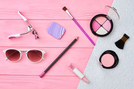 Flat lay female essentials, color background. Sunglasses, lipstick, eyeshadows, blusher. Woman beauty accessories set.の写真素材