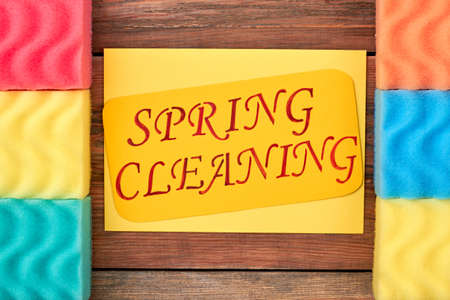 Frame from kitchen sponges on wooden background. Two rows of multicolored kitchen sponges with paper card in the middle. Necessity of spring cleaning.の写真素材