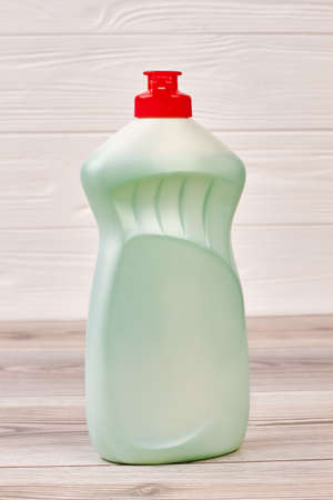 Bottle with liquid for dish washing. Green plastic detergent with red cap close up. Eco-cleaning...