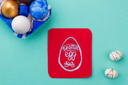 Painted Easter eggs in paper container. Easter egg drawn on paper card. Styrofoam eggs on blue background. Symbols of Easter holidays.の写真素材