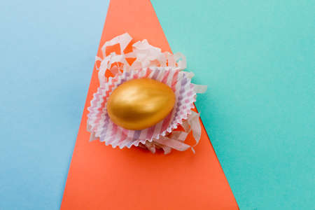 Golden egg on colorful background. Golden chicken Easter egg in paper wrap. Symbol of happy Easter.の写真素材