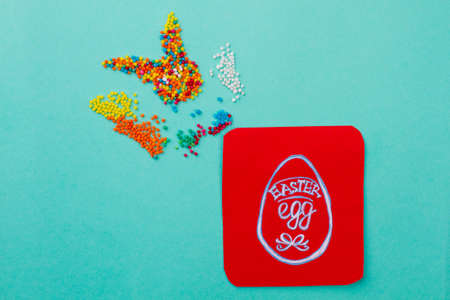 Colorful candies shaping a rabbit. Colorful sweets and image of Easter egg on red paper card. Easter...