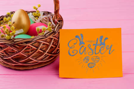Wicker basket with colorful Easter eggs. Golden egg among colorful Easter eggs in basket. Easter greeting card on pink background.の写真素材