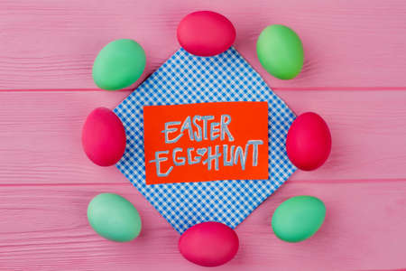Composition from Easter eggs on pink background. Colorful Easter eggs, paper card with text Easter egg hunt, top view.の写真素材
