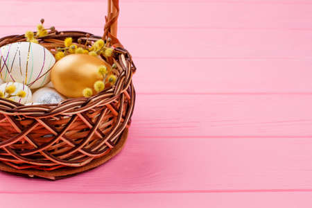 Easter eggs in wicker basket. Gold egg, decorated styrofoam egg and pussy willow in woven basket on pink wood, copy space. Happy Easter background.の写真素材
