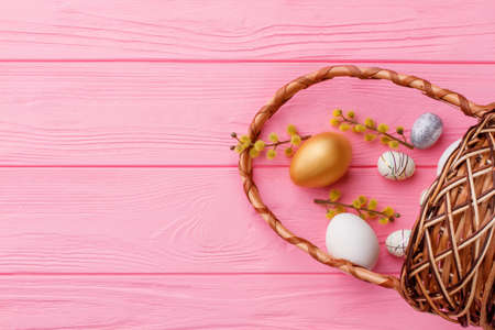 Still life Easter composition. Decorative Easter eggs, pussy willow twigs and basket on pink wooden background, space for text.の写真素材