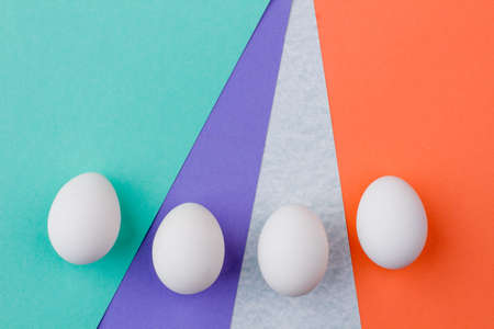 Four white Easter eggs. Group of uncooked Easter eggs on multicolored paper background with space for text. Easter art minimal.の写真素材