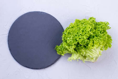 Green lettuce and natural slate board. Dark gray slate stand and fresh green lettuce salad, top view. Restaurant utensil and organic food.の写真素材