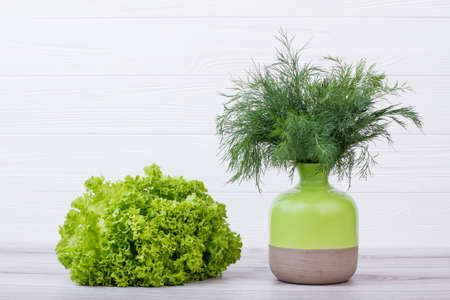Bouquet of dill in ceramic pot. Bunch of dill in two-tone ceramic vase. Fresh lettuce on wooden background. Concept of organic food.の写真素材