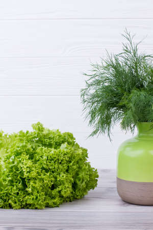Beautiful composition with green herbs. Fresh lettuce on wooden background. Bouquet of dill in two-tone ceramic vase. Vegan food concept.の写真素材