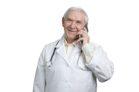 Old caucasian doctor is talking on the phone in a great mood. Portrait of smiling physician having conversation using smartphone. White isolated background.の写真素材