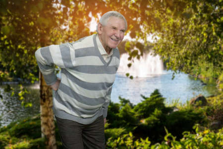 Old man with backache outdoor. Senior grandfather suffering from back pain in the park.