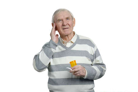 Sick senior man with headache and bottle of pills. Old man taking pills to reduce head pain, white isolated background.の写真素材