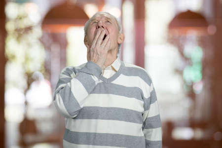 Portrait of yawning senior. Caucasian old man is yawning, abstract blurred background.の写真素材
