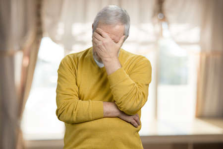 Portrait of old grandpa doing facepalm. Forgetful old man holding his hand to his forehead.の写真素材