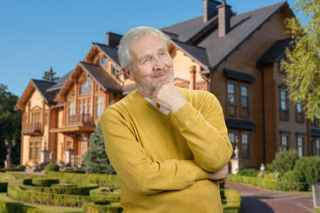 Portrait of old thoughtful grandfather. Rich senior man thinking on his big house background.の写真素材