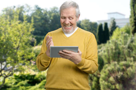 Senior man with tablet pc computer on trees background. Technology, people and lifestyle concept. Happy old man with gadget.の写真素材
